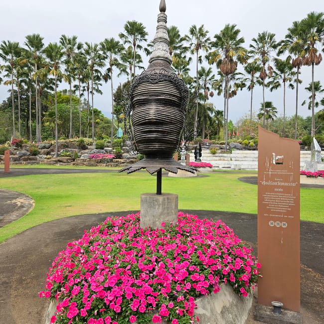Rzeźba w royal park rajapruek w chiang mai otoczona różowymi kwiatami i palmami