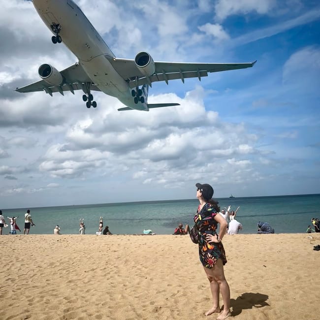 Samolot nisko przelatuje nad plażą w phuket, a turyści obserwują lądowanie.