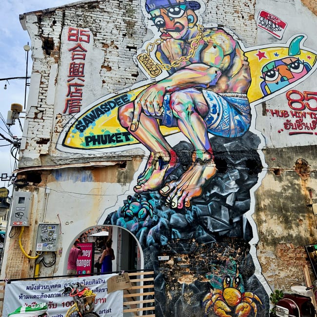 Mural street art w phuket, przedstawiający kolorową postać na zniszczonej ścianie budynku.