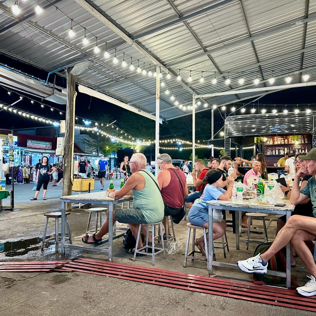 Phuket naka weekend market w phuket nocą, z ludźmi siedzącymi przy stołach pod lampkami.