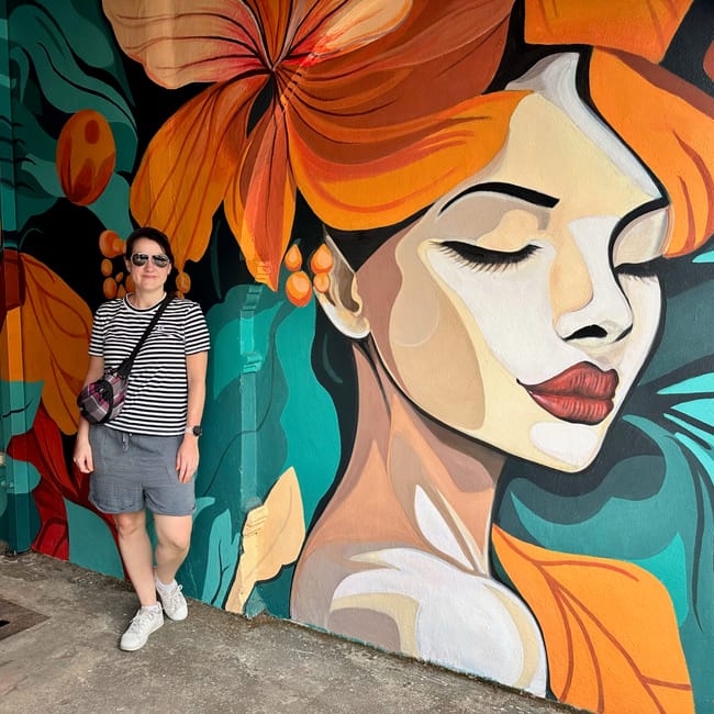 Phuket old town w tajlandii: kobieta stoi przy kolorowym muralu z twarzą i dużymi pomarańczowymi kwiatami.
