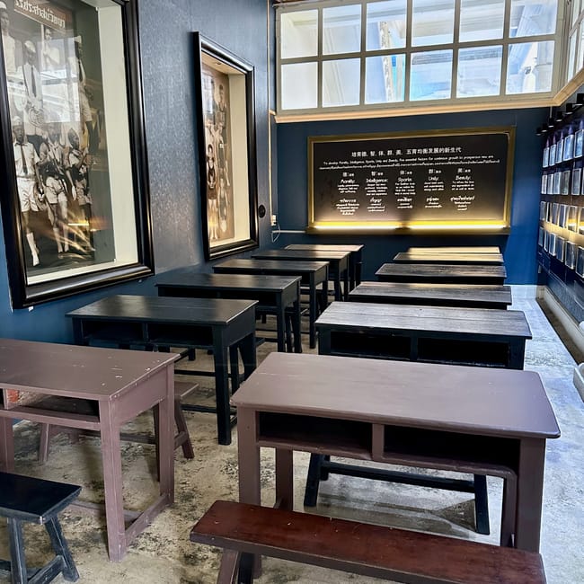 Wnętrze phuket thai hua museum z rzędami szkolnych ławek i historycznymi fotografiami.