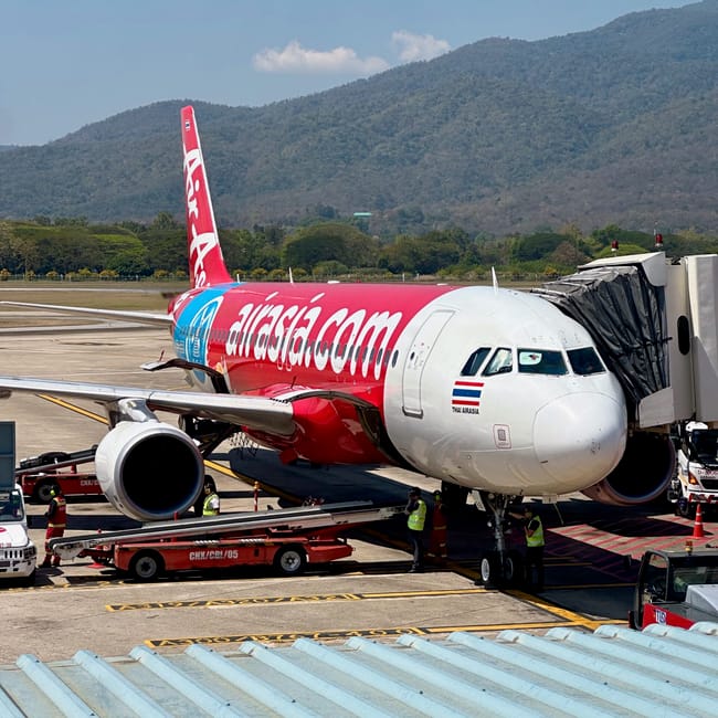 Samolot thai airasia przy rękawie na lotnisku w phuket, z górami w tle.