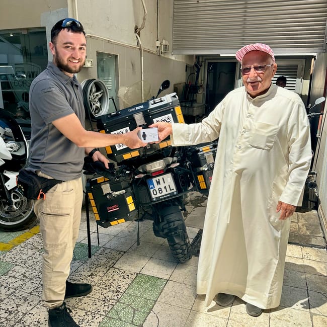 Desert horizons motorcycle expedition, kuwait: two men in a garage holding motorcycle registration papers in front of bikes
