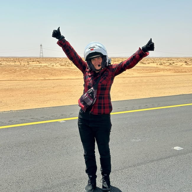 Motocyklistka w kasku stoi na pustynnej drodze w al ula w arabii saudyjskiej, z uniesionymi kciukami.