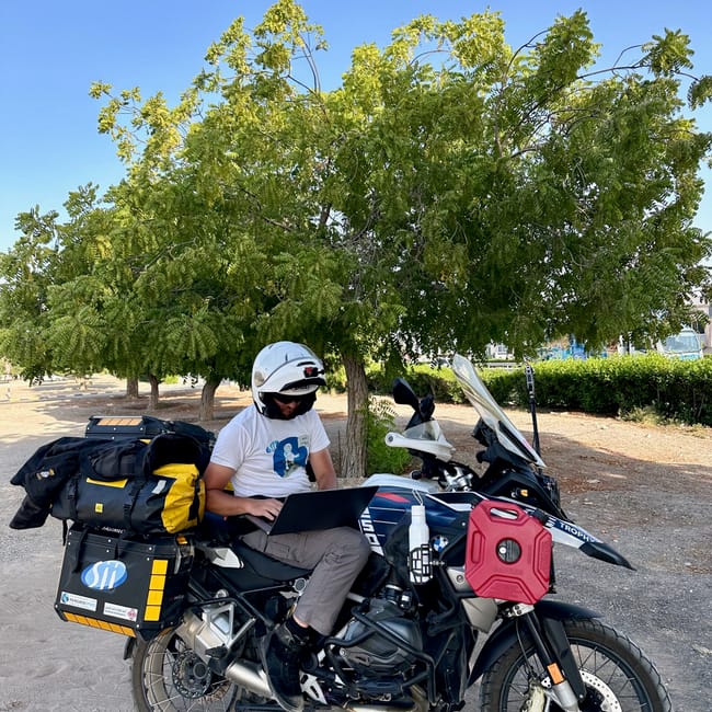 Motocyklista z bagażem na wyprawie desert horizons w omanie, siedzący na motocyklu pod drzewami.