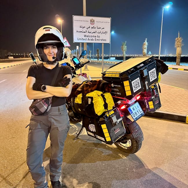 Motocyklistka przy znaku „welcome to united arab emirates” podczas nocnej wyprawy przez emiraty