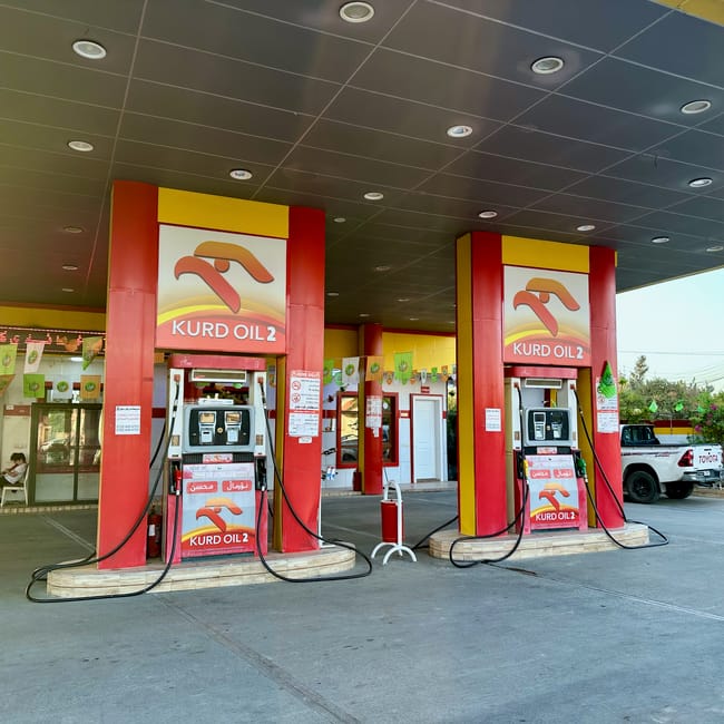 Stacja benzynowa kurd oil 2 w kurdystanie, z czerwono-żółtymi dystrybutorami pod zadaszeniem.