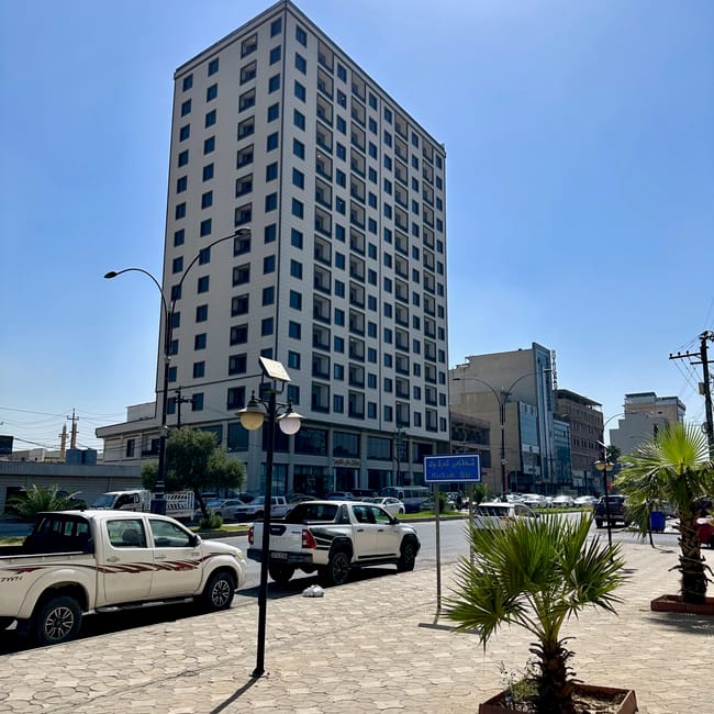Hotel erbil w iraku przy ulicy kirkuk, z zaparkowanymi samochodami i palmami na chodniku