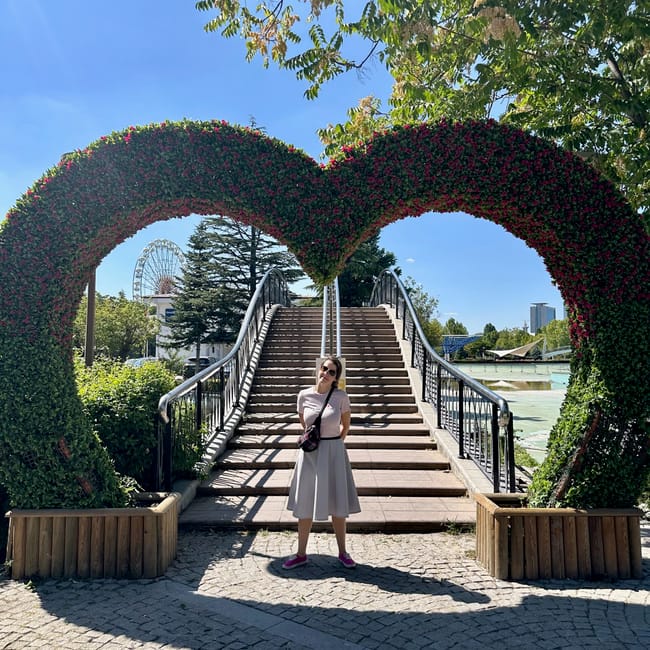 Turkey, ankara genclik park: archway covered with flowers framing stairs by the lake with a woman standing in sunlight