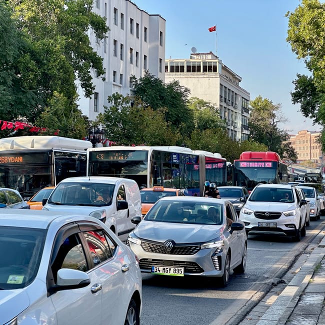 Ulica w ankarze z korkiem samochodowym, autobusami i tureckimi flagami.
