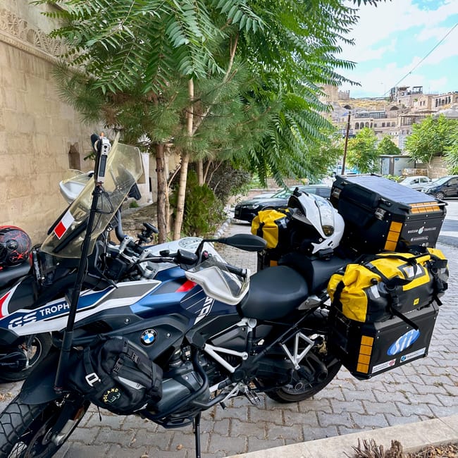 Motocykl bmw gs w kapadocji, zaparkowany przy ulicy z kuframi podróżnymi.