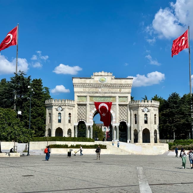 Brama uniwersytetu stambulskiego na placu beyazıt w stambule, z tureckimi flagami i wieżą w tle