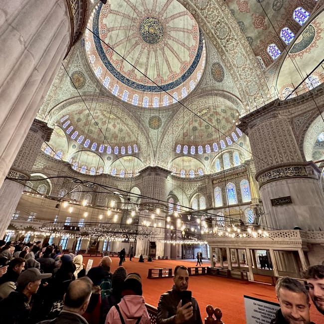 Wnętrze meczetu sultanahmet camii w stambule z kopułami, witrażami i zwiedzającymi.