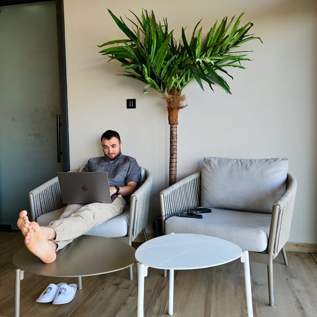 Kuwait hotel lounge in filip in hotel: man relaxing on a sofa using a laptop, with a tall palm plant nearby