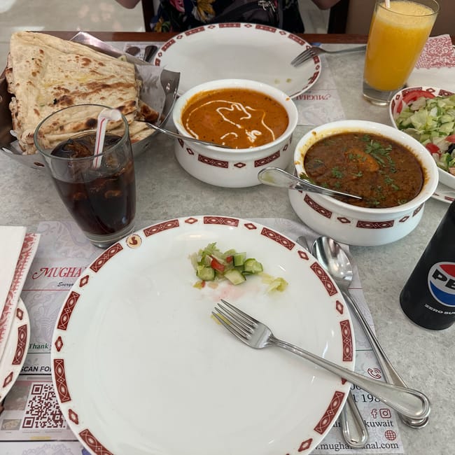 Kuwait foods table with flatbread, two bowls of soup, salad, orange juice, and tea glasses