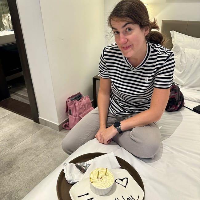Jadzia in kuwait holds a gift near a happy birthday cake with candles on a hotel bed
