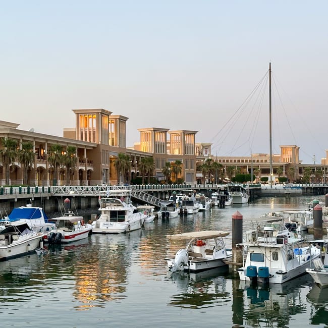 Boats docked along kuwait’s city souq sharq marina with a tall mast and waterfront buildings.