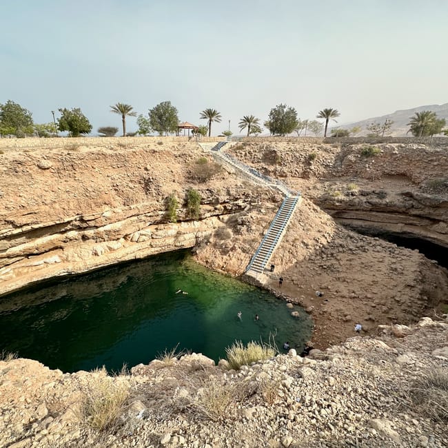 Dabab bimmah sink hole w omanie, wapienny lej z zieloną wodą i schodami prowadzącymi na dół