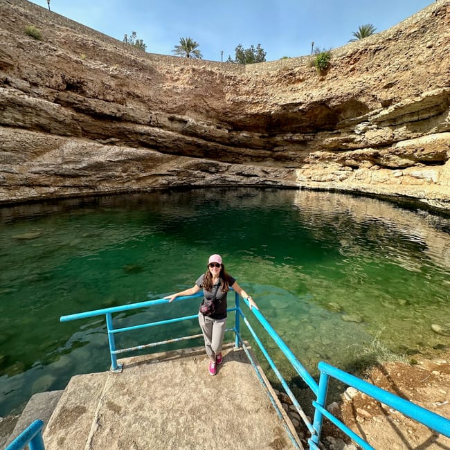 Kobieta na platformie nad zieloną wodą w dabab bimmah sink hole w omanie, otoczoną skalnymi ścianami.