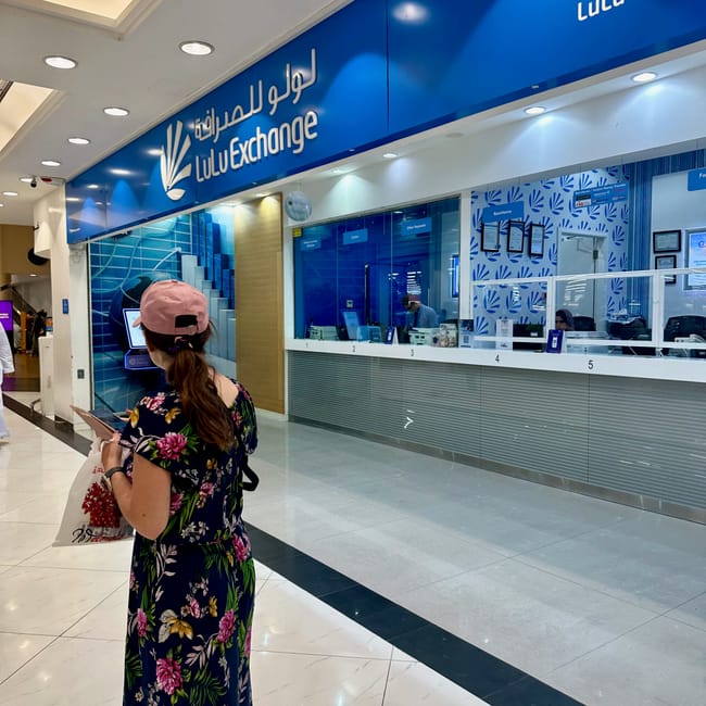 Kantor lulu exchange w centrum handlowym w muskacie, z ladami obsługi i kobietą stojącą przed wejściem.
