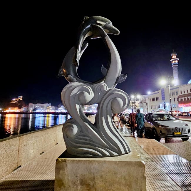 Rzeźba delfinów na muttrah corniche w muskacie nocą, przy nadmorskiej promenadzie i oświetlonych budynkach