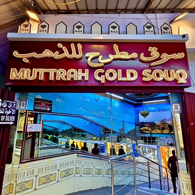 Wejście do muttrah gold souq w muskacie, z podświetlanym szyldem i schodami prowadzącymi do wnętrza.