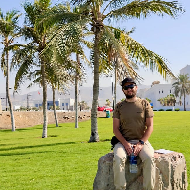 Mężczyzna siedzący na kamieniu wśród palm na trawniku przy plaży qurum w maskacie, oman.