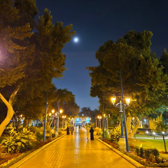 Nocny deptak w muscat qurum natural park w omanie, oświetlony latarniami, wśród drzew i pod księżycem.