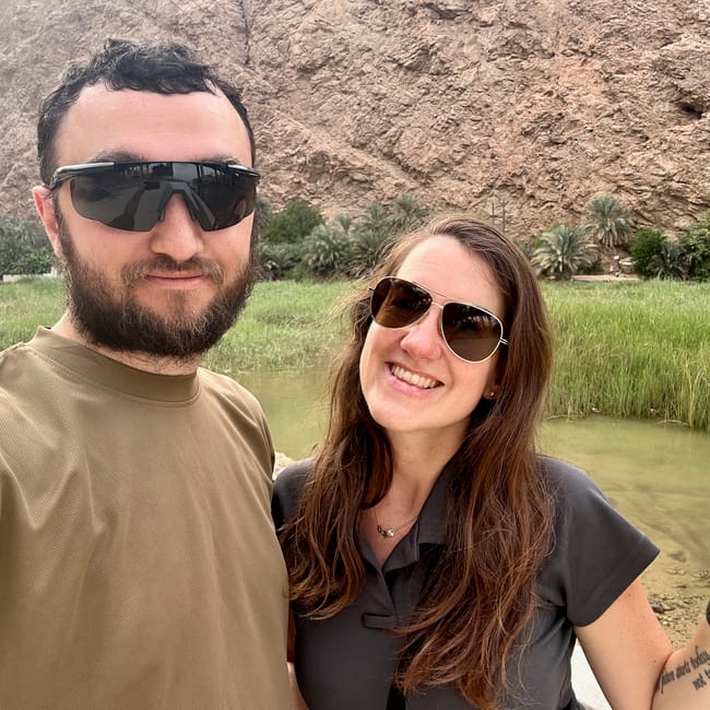 Para turystów robi selfie w wadi shab w omanie, na tle skał, palm i zielonej wody.