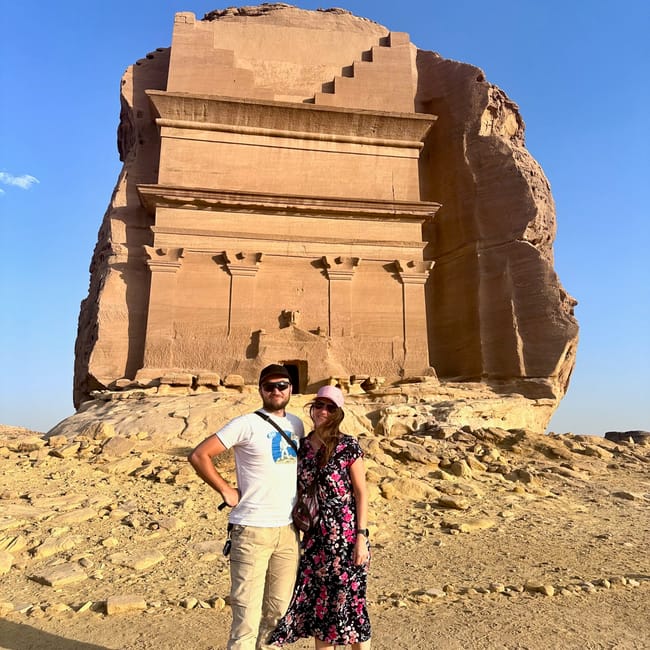 Couple posing in front of a large sandstone monument at al ula hegra, saudi arabia