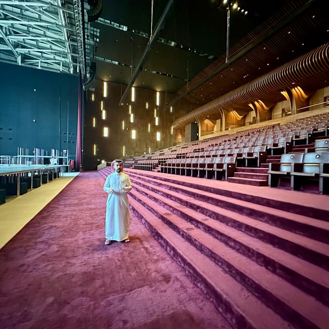 Saudi arabia, al ula maraya: a man in white robes standing inside a modern theater auditorium at night