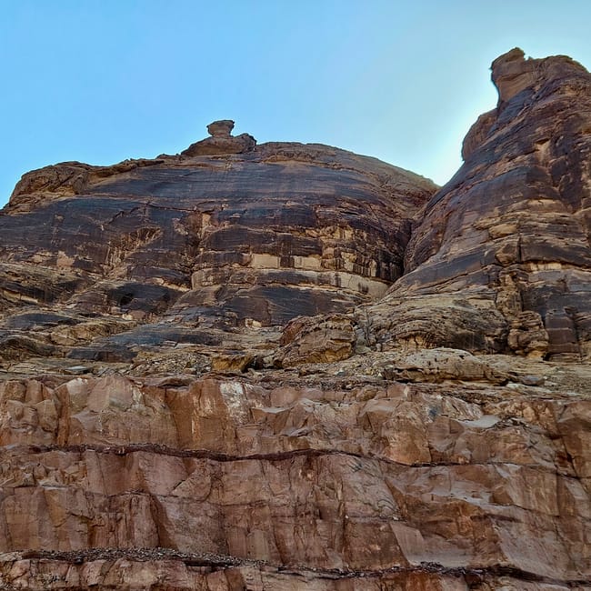 Saudi arabia, al ula old town: rugged sandstone cliffs with a small stone structure at the base under a blue sky