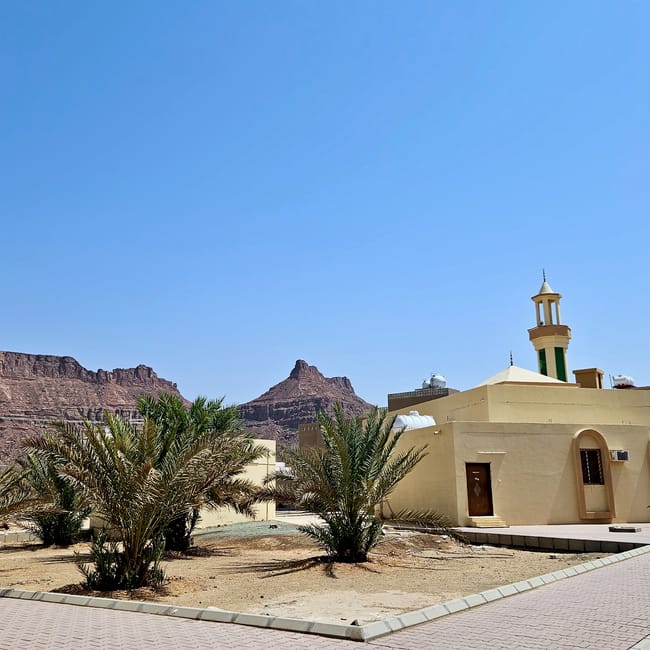 Al ula, saudi arabia mosque with palm trees and desert cliffs in the background