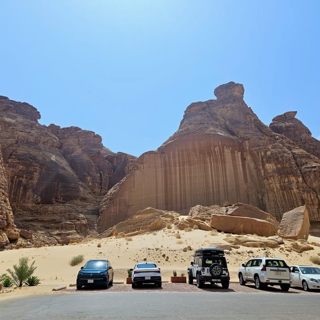 Al ula, saudi arabia: cars parked on a road before towering desert rock formations