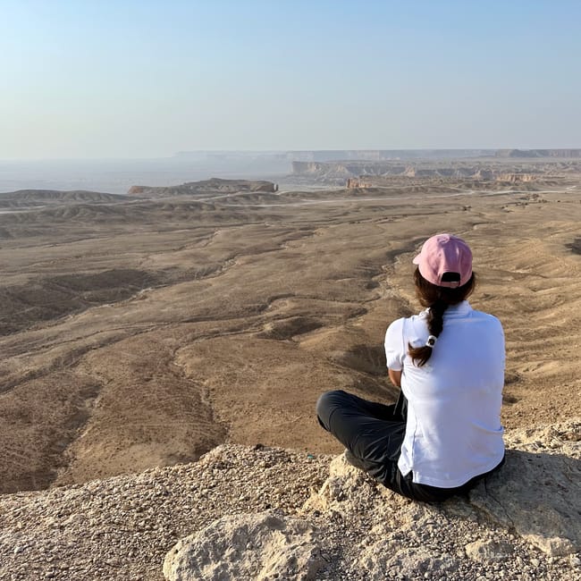 Woman sitting on a rocky viewpoint overlooking edge of the world in saudi arabia