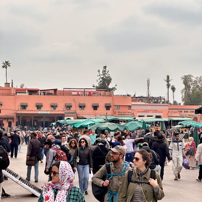 Crowds at jemaa el-fnaa in marrakesh, morocco, with green market stalls and travelers in the plaza