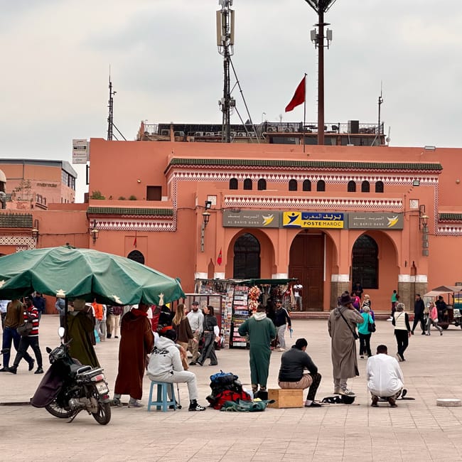 People gather in marrakesh at jemaa el-fnaa in front of a red bank building.