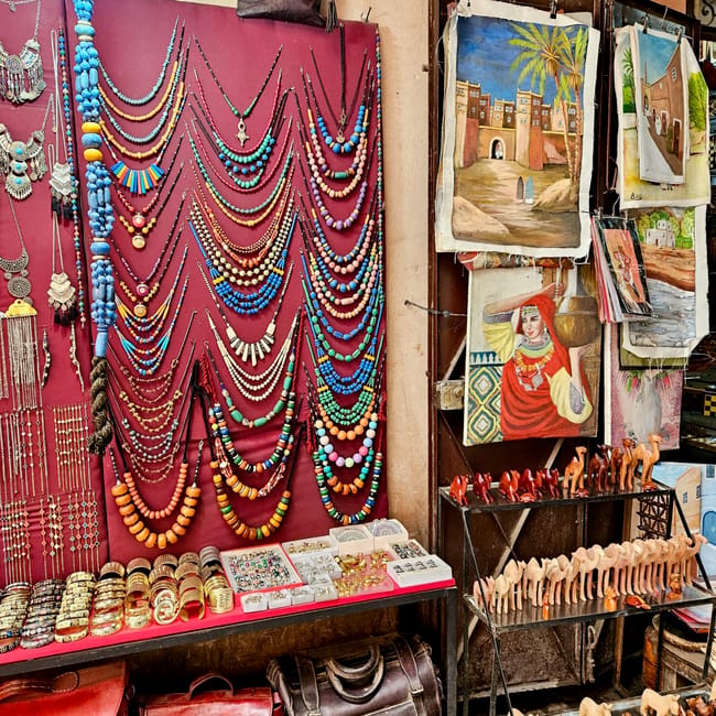 Souk semmarine in marrakesh, morocco: colorful bead necklaces, leather bags, and hanging artworks in a shop.