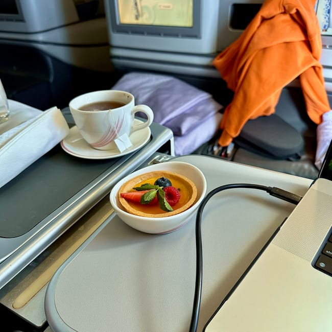 Posiłek w biznes klasie air china: filiżanka herbaty i tarta owocowa na rozkładanym stoliku przy fotelu