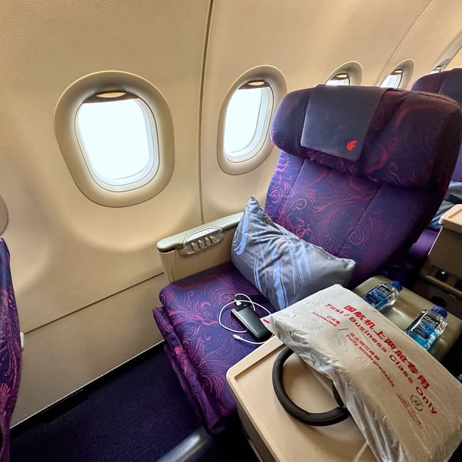 Kabina klasy biznes air china z fioletowymi fotelami przy oknie i zestawem pokładowym