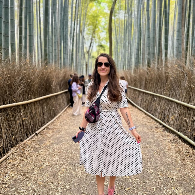 Woman in sunglasses and a polka-dot dress standing on a path through a bamboo grove