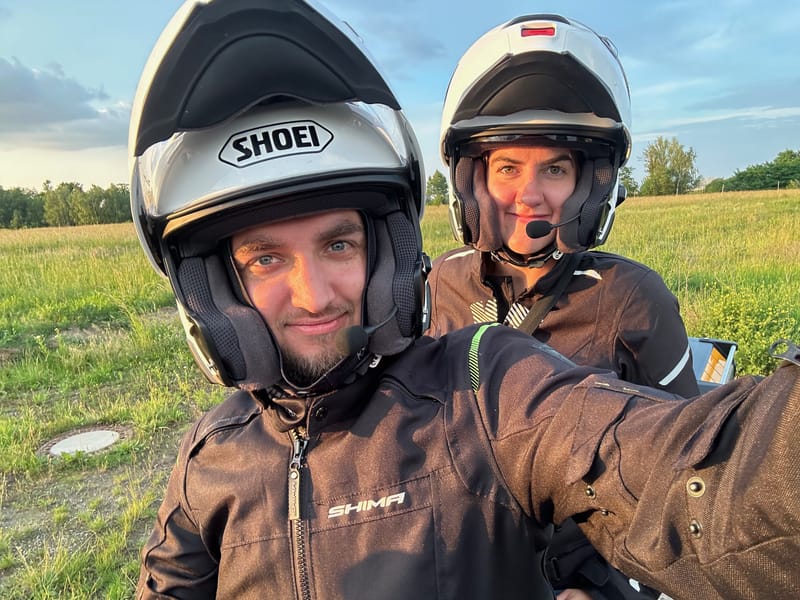 Dwoje motocyklistów w kaskach robi selfie na łące o zachodzie słońca.