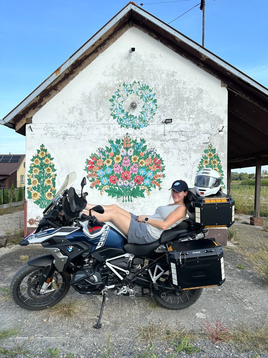 Rowerzystka na motocyklu przed malowaną kwiatami chatą w zalipiu.