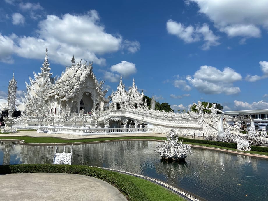 Biała świątynia wat rong khun w chiang rai, odbijająca się w stawie pod błękitnym niebem.