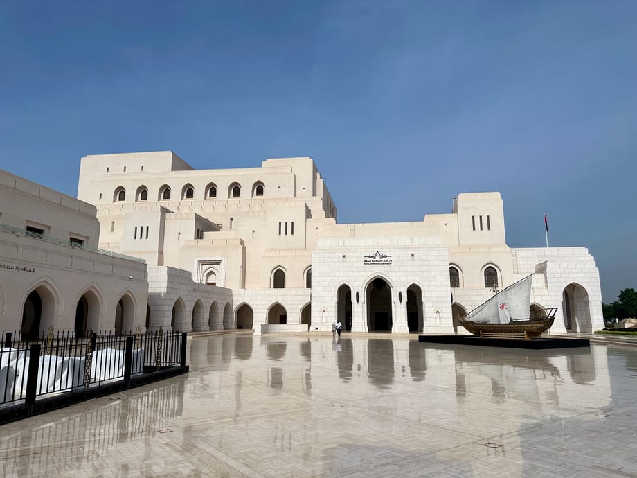 Royal opera house muscat w omanie, jasny gmach z arkadami i łodzią na dziedzińcu po deszczu