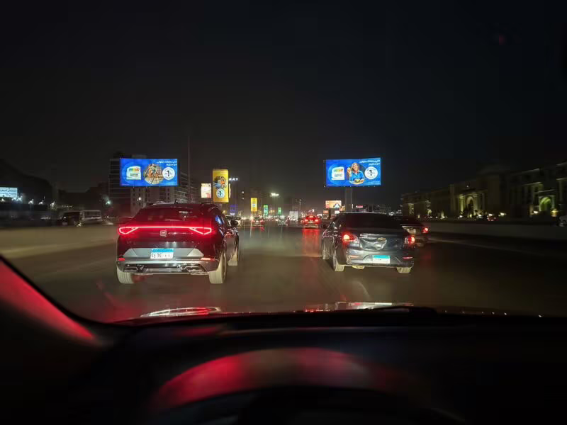 Nocny ruch na alei safety w egipcie, widziany z samochodu, z reklamami i światłami aut.
