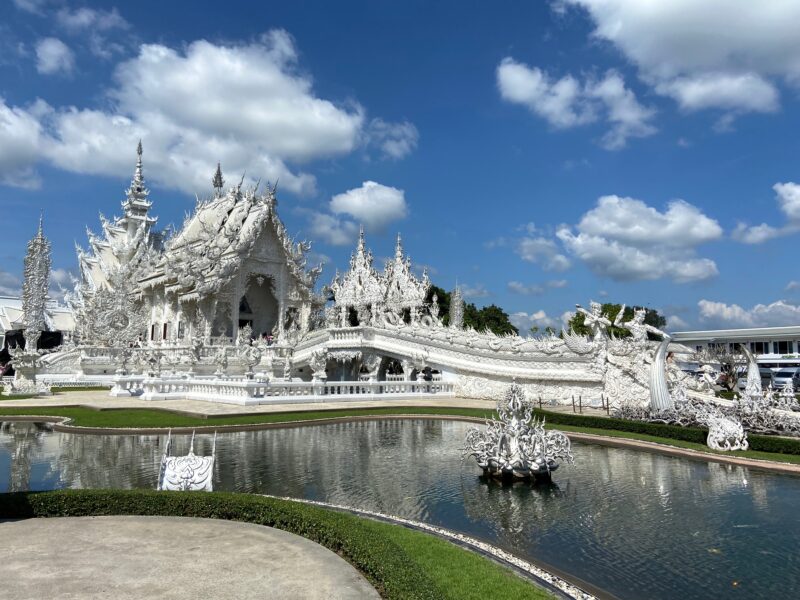Biała świątynia wat rong khun w chiang rai, odbijająca się w stawie pod błękitnym niebem.