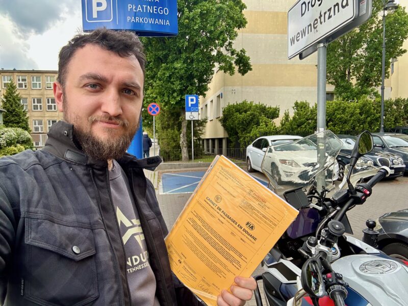 Mężczyzna z motorem trzyma carnet de passage na ulicy w warszawie.