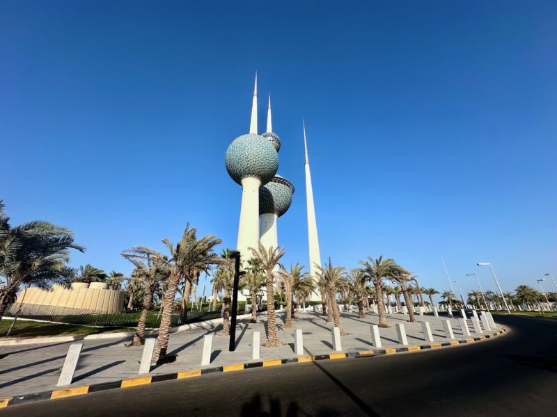 Wieże kuwait towers w kuwejcie, otoczone palmami pod bezchmurnym niebem.
